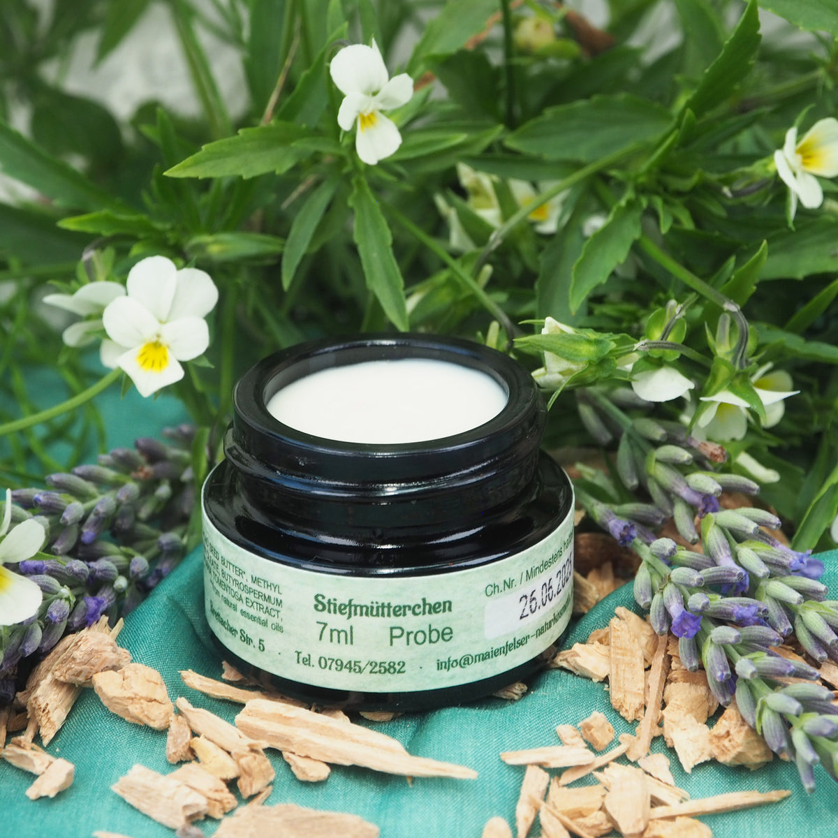 Geöffneter 7ml Stiefmütterchen Creme Tiegel. Im Hintergrund sind Stiefmütterchen.