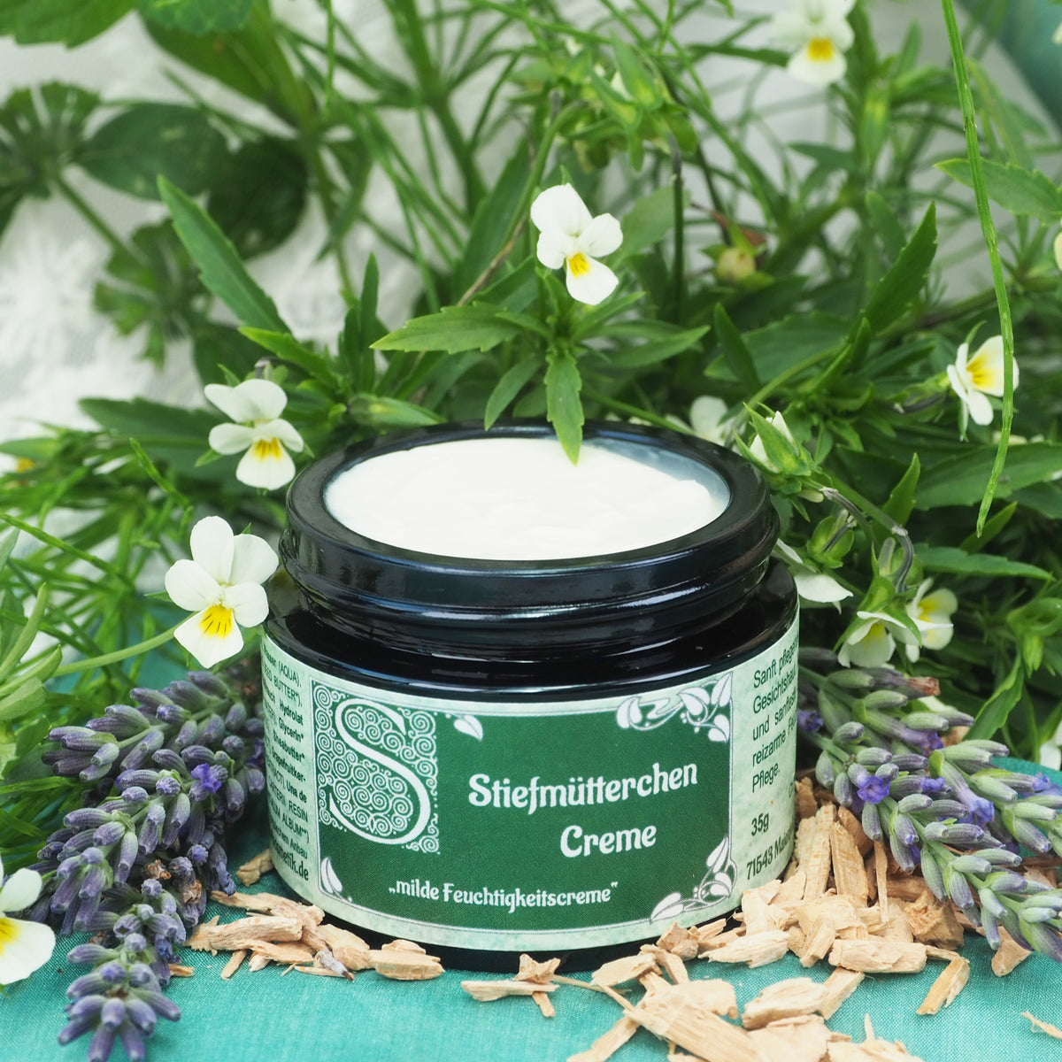 Geöffneter 35ml Stiefmütterchen Creme Tiegel. Im Hintergrund sind Stiefmütterchen.