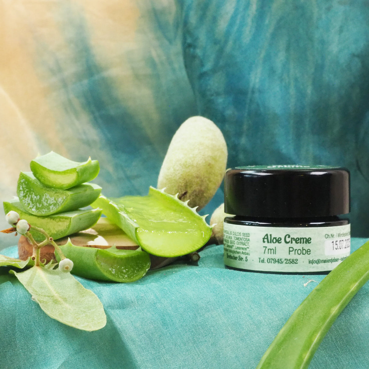 Aloe Creme 7ml Tiegel, daneben liegen Aloe Blätter.